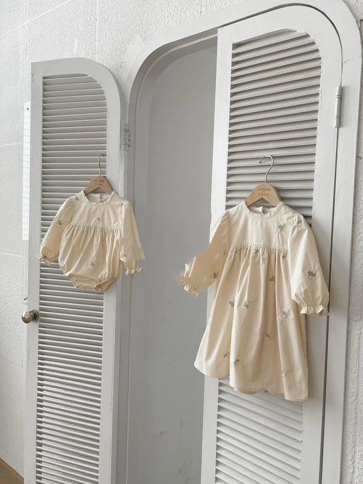 Cream-colored baby dress with long sleeves and floral embroidery hanging on white shutter door