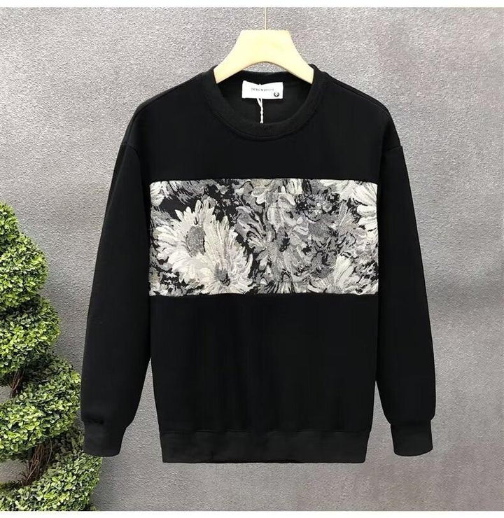Black sweatshirt with gray and white floral embroidered panel across chest on wooden hanger