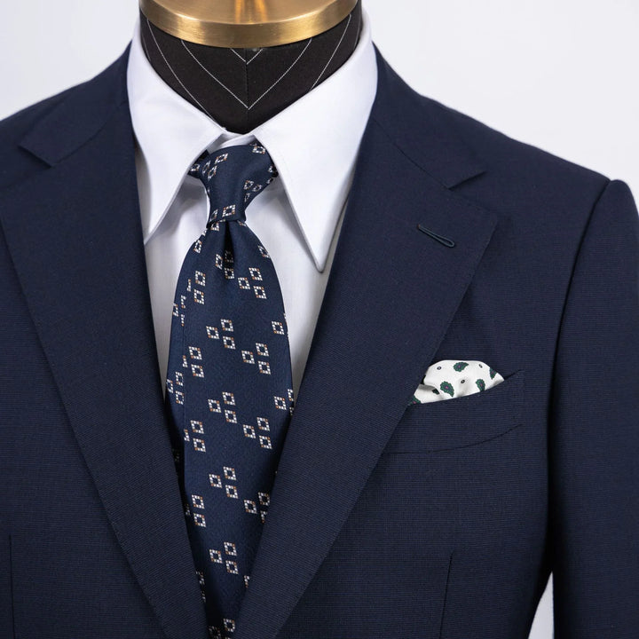 Close-up of navy blue suit jacket with white dress shirt, patterned navy tie, and white pocket square on mannequin