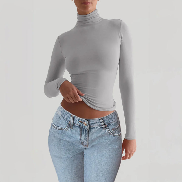 woman wearing a fitted light gray turtleneck long sleeve top and light blue high-waisted jeans