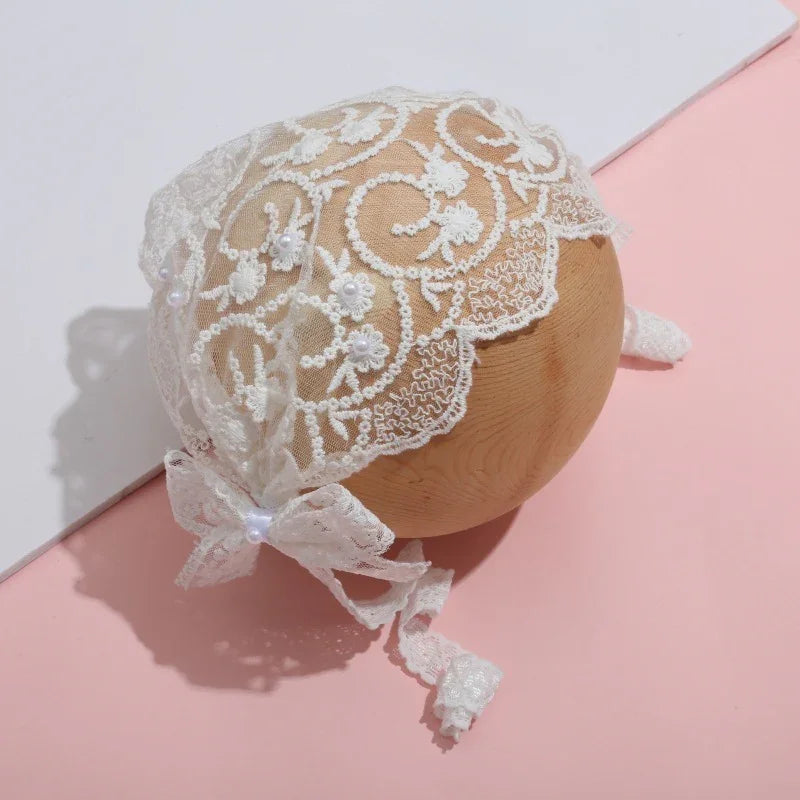 Delicate white lace baby bonnet with floral embroidery and bow on wooden sphere, pink and white background