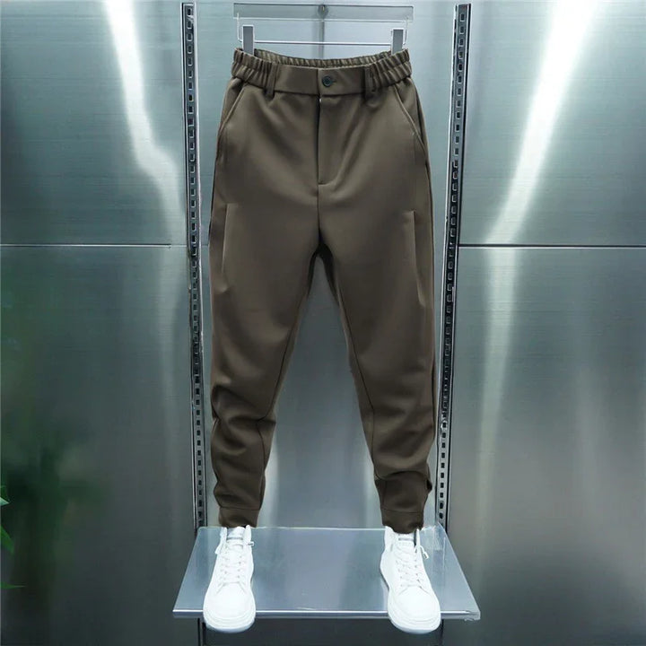 Brown tapered jogger pants with elastic waistband and button, paired with white sneakers on metal display