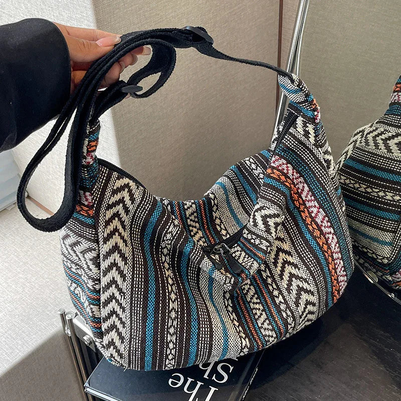 Hand holding a woven boho shoulder bag with black, blue, white, and orange striped pattern on a dark surface