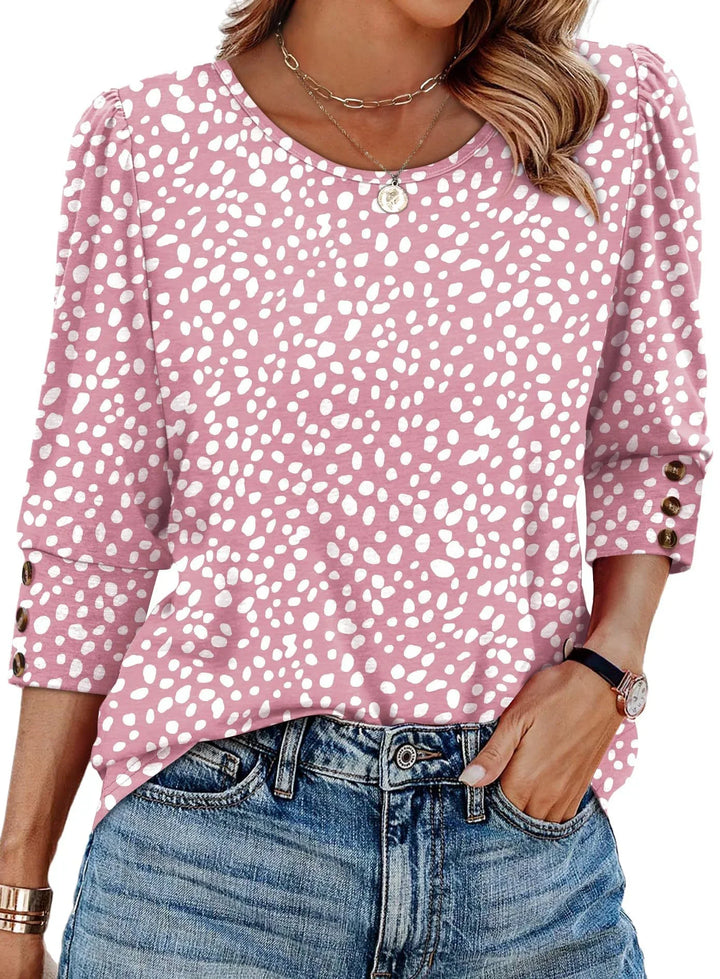 Woman wearing a pink and white spotted blouse with 3/4 sleeves and button details, paired with blue denim jeans