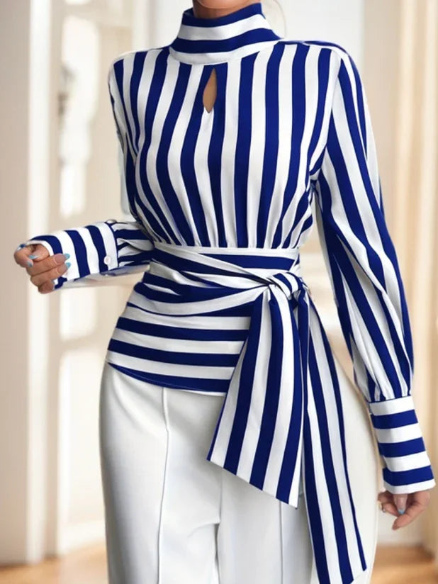 Woman wearing blue and white vertical striped blouse with tied waist belt and white pants