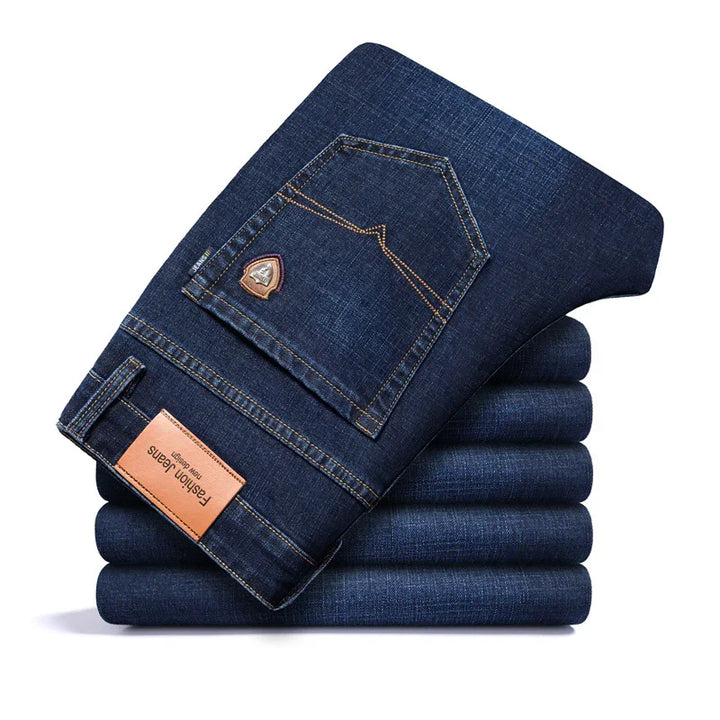 Folded stack of dark blue denim jeans with back pocket detail and brown fashion jeans label
