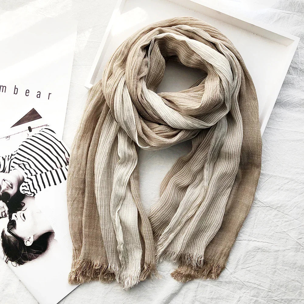 Soft beige and white striped textured scarf with fringed edges displayed on a white fabric surface