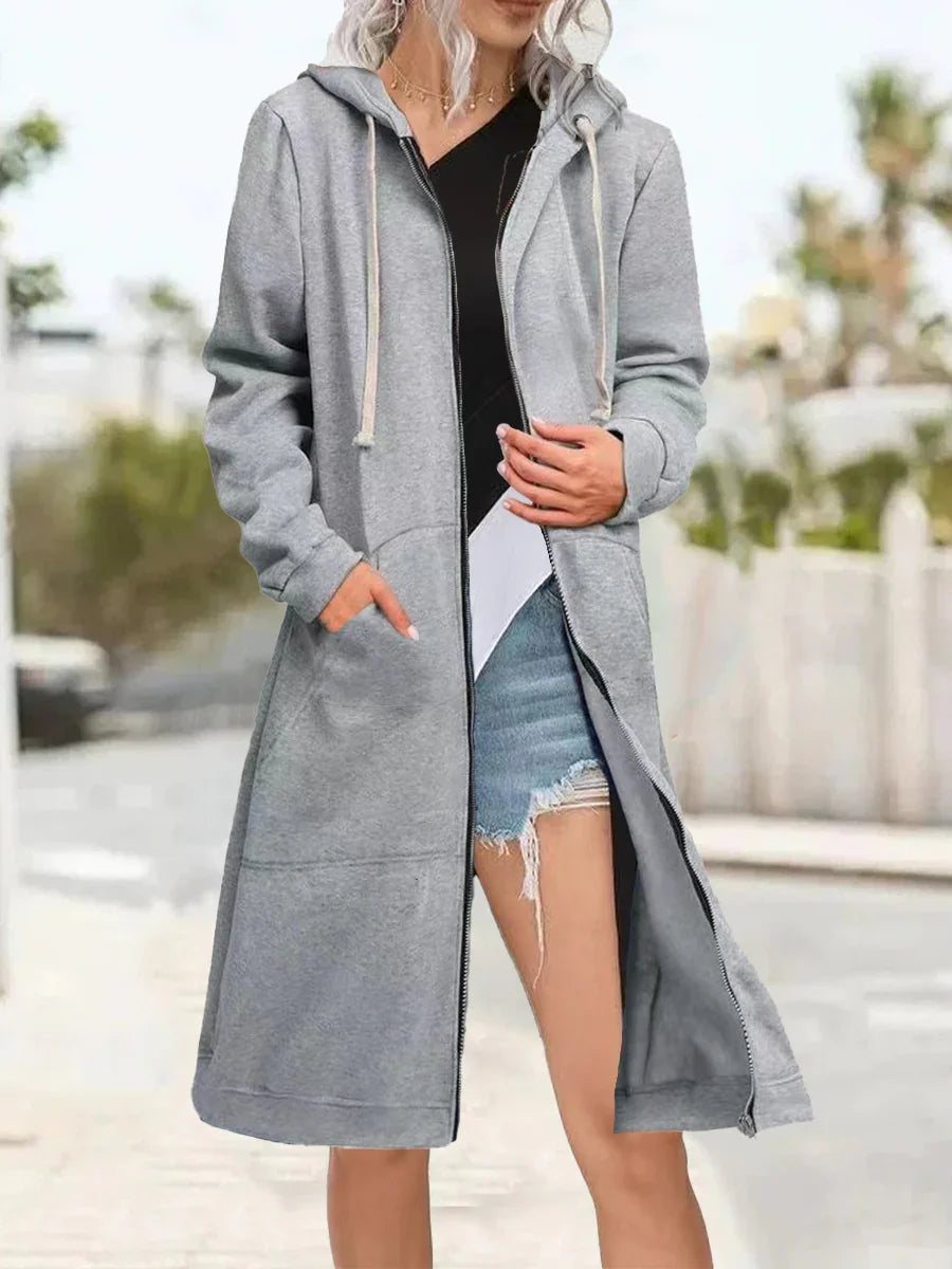 Woman wearing long gray zip-up hoodie with hood and pockets over black top and ripped denim shorts outdoors