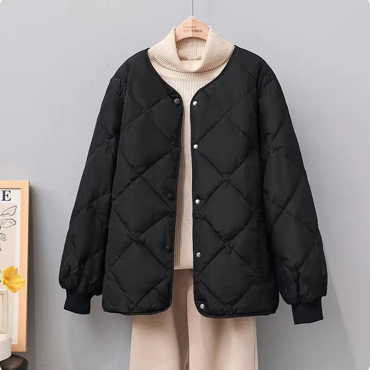 Black quilted button-up jacket on hanger over beige turtleneck sweater and pants against gray wall