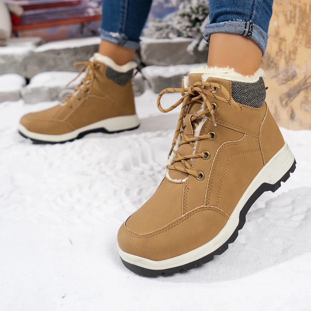 Close-up of tan winter boots with fur lining on snow, worn with rolled blue jeans