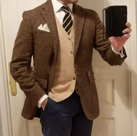 Man wearing a brown tweed blazer, beige cardigan, white shirt, striped tie, and navy pants taking a mirror selfie