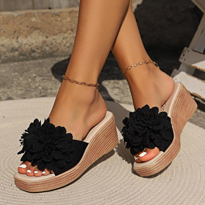 Woman wearing black floral wedge sandals with ankle chains on outdoor rug