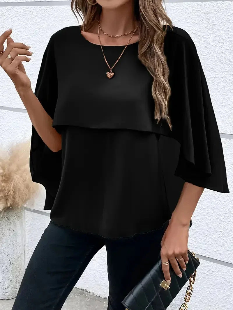 woman wearing black layered top with loose sleeves, gold heart necklace, holding black quilted clutch bag
