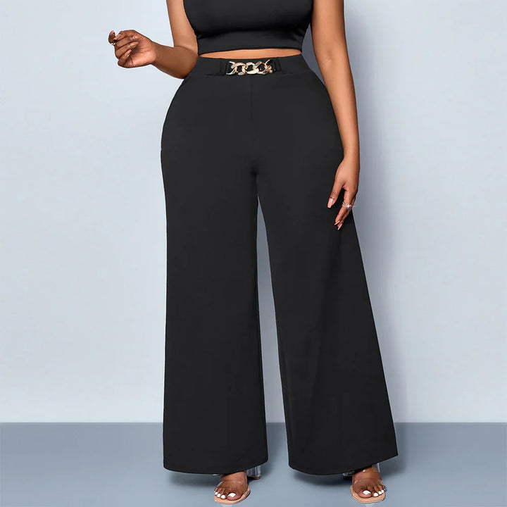 Woman wearing high-waisted black wide-leg pants with gold chain belt and black crop top