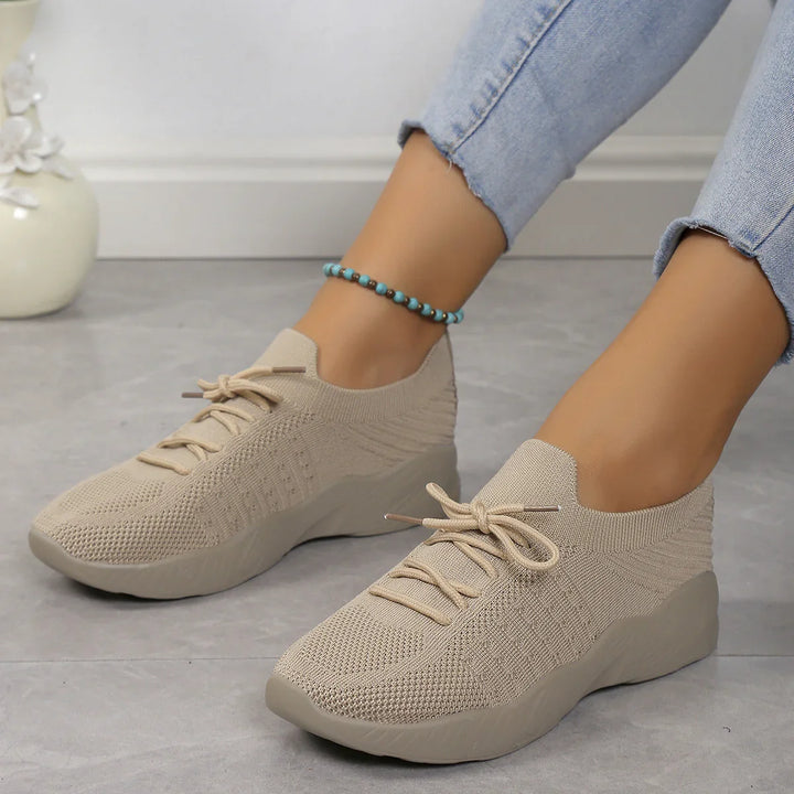 Beige knitted casual sneakers with lace-up design worn with light blue jeans on gray floor