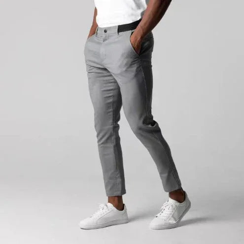 Man wearing slim fit gray chinos with white sneakers and a white t-shirt on plain background