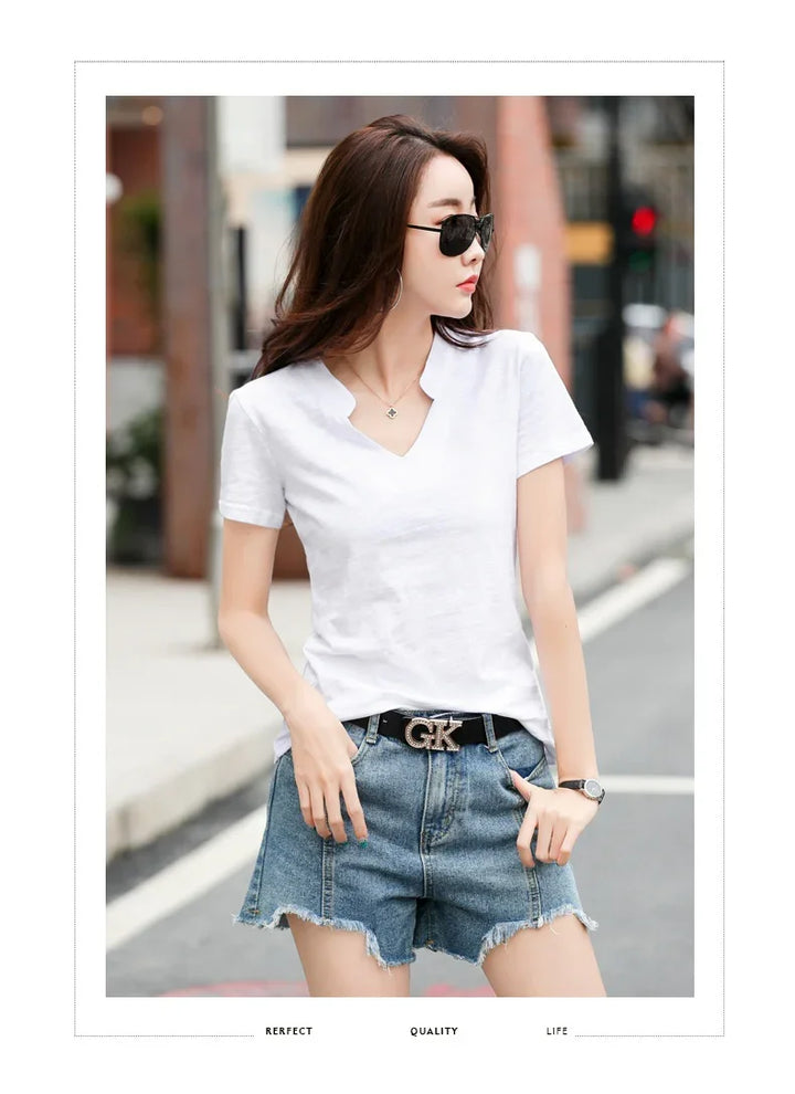 Woman wearing white V-neck T-shirt, denim shorts with GK belt, black sunglasses, and watch on city street