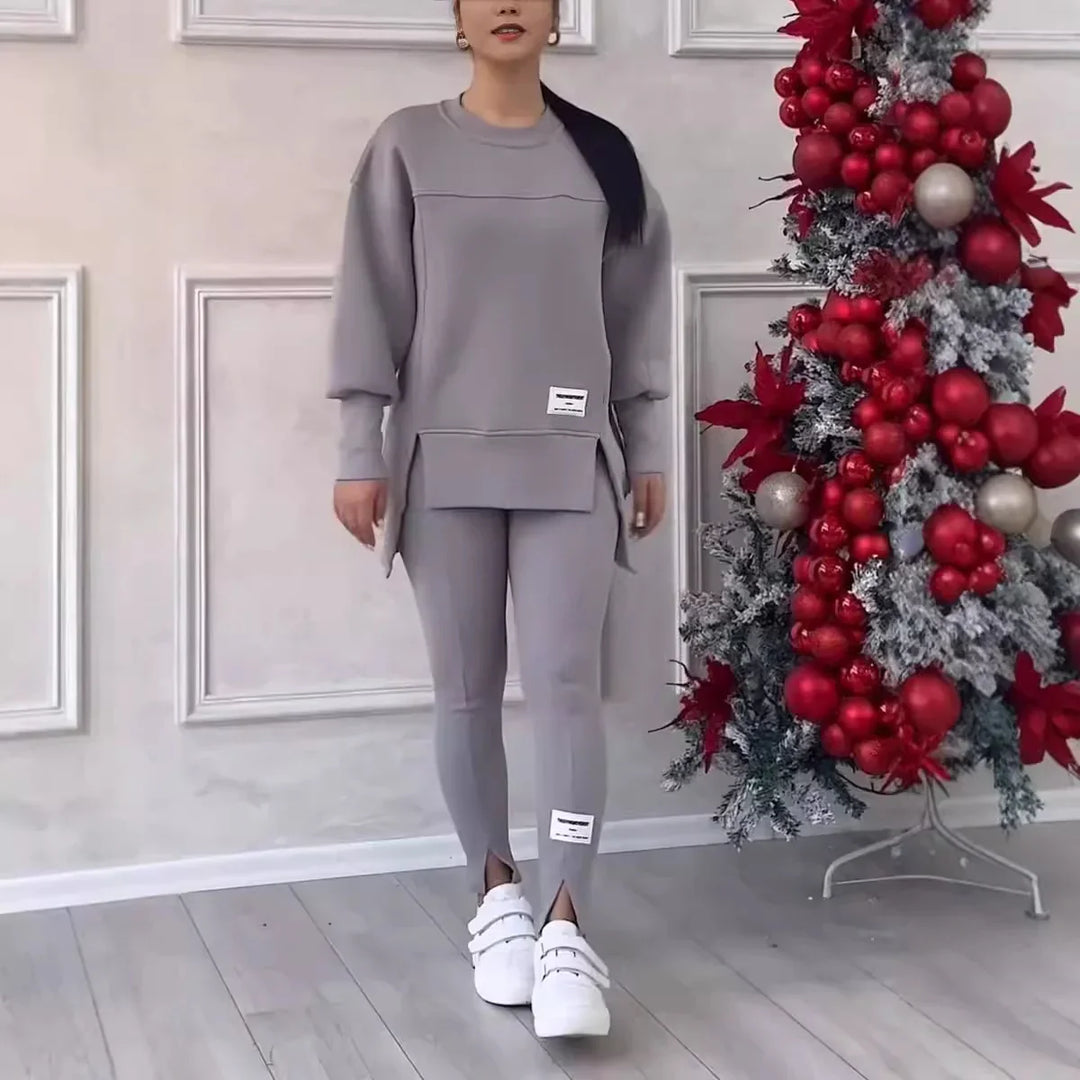 Woman wearing gray matching casual sweatshirt and leggings standing next to flocked Christmas tree with red ornaments