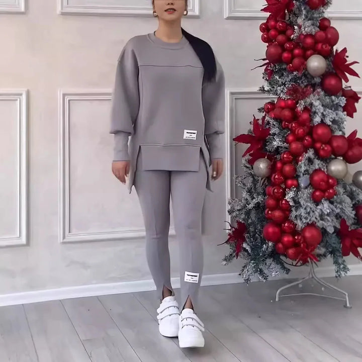 Woman wearing gray matching casual sweatshirt and leggings standing next to flocked Christmas tree with red ornaments