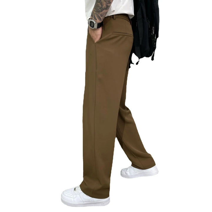 Man wearing brown straight-leg trousers, white sneakers, and a white shirt, side view
