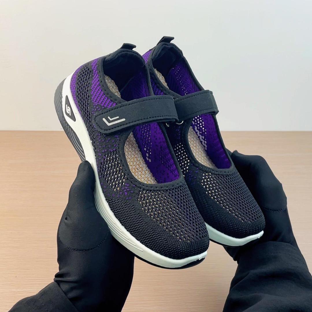 hands holding black and purple mesh athletic shoes with white soles and velcro straps