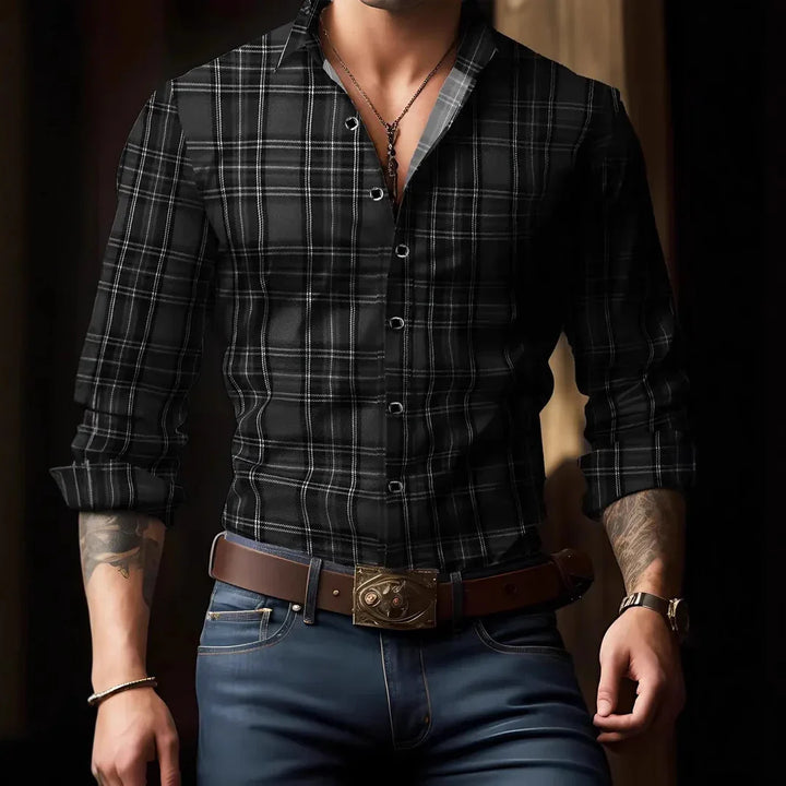 Man wearing black plaid button-up shirt with rolled sleeves, brown belt, blue jeans, and accessories