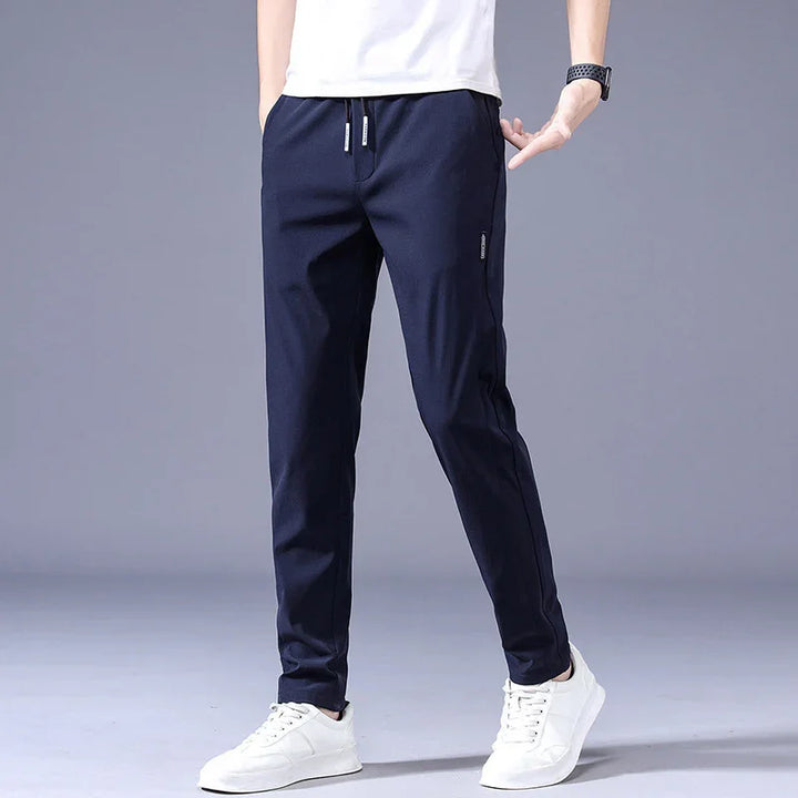 Man wearing navy blue slim-fit jogger pants with drawstring and white sneakers on grey background