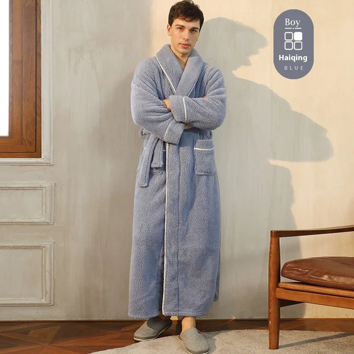 Man wearing long blue plush bathrobe with white piping, standing indoors by wooden chair and window