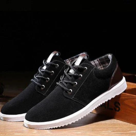 Black casual men's shoes with white soles and plaid inner lining on wooden surface