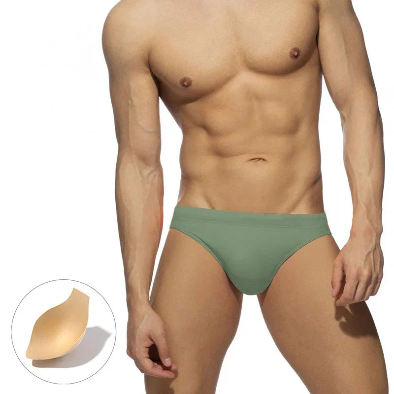 Muscular male torso wearing green bikini briefs with detachable padded inserts on white background