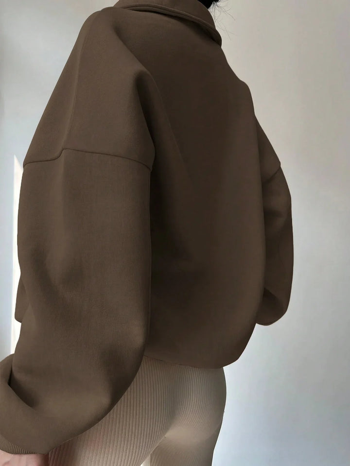 Person wearing oversized brown sweater and cream ribbed pants in minimalist setting