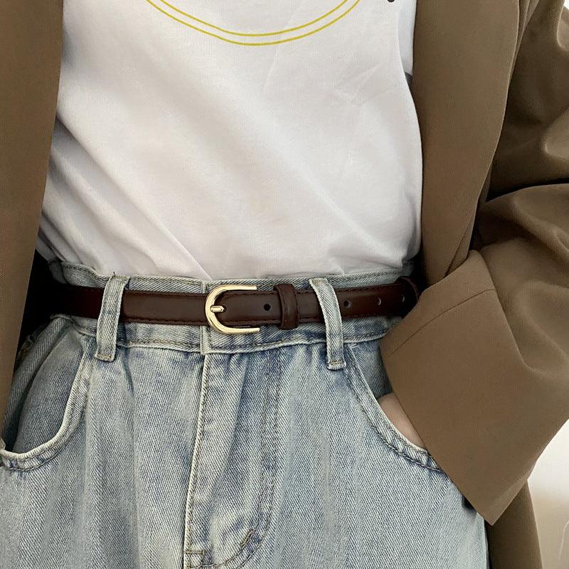 Close-up of casual outfit featuring light blue denim jeans with brown leather belt and white t-shirt under brown blazer