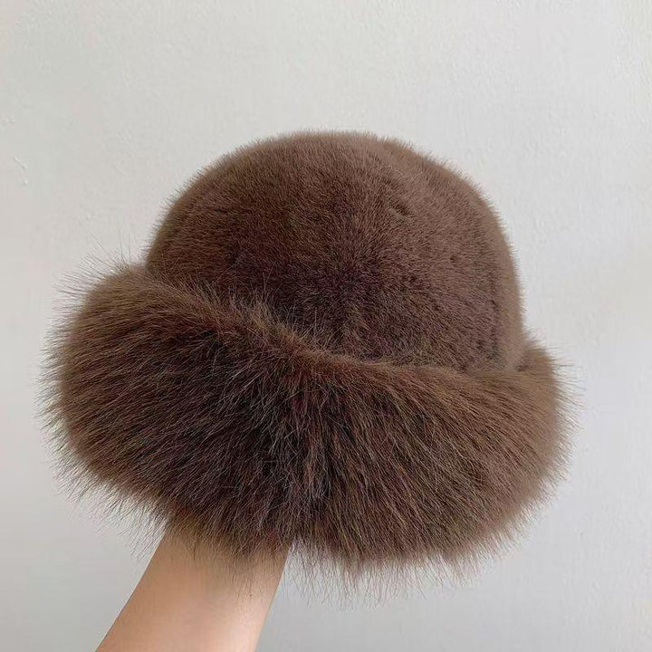 hand holding a soft brown fur hat with a fluffy trim against a plain white background