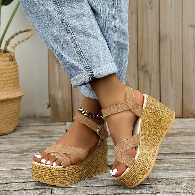 Close-up of feet wearing tan suede platform wedge sandals with ankle straps, paired with cuffed light blue jeans on wooden floor