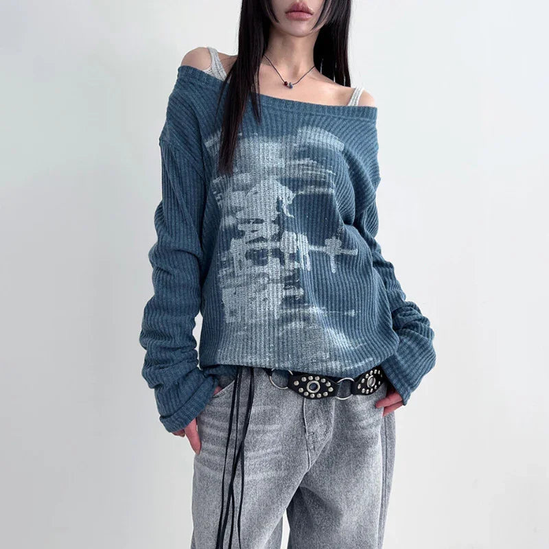 Woman wearing off-shoulder blue ribbed sweater with white abstract print and gray loose jeans with studded black belt