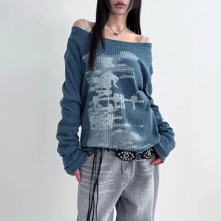 Woman wearing off-shoulder blue ribbed sweater with white abstract print and gray loose jeans with studded black belt