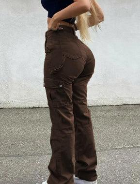 woman in brown cargo pants and black top standing on street with gray wall background