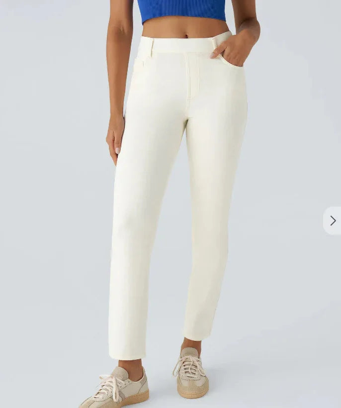 Woman wearing white slim-fit pants with pockets and beige sneakers against gray background