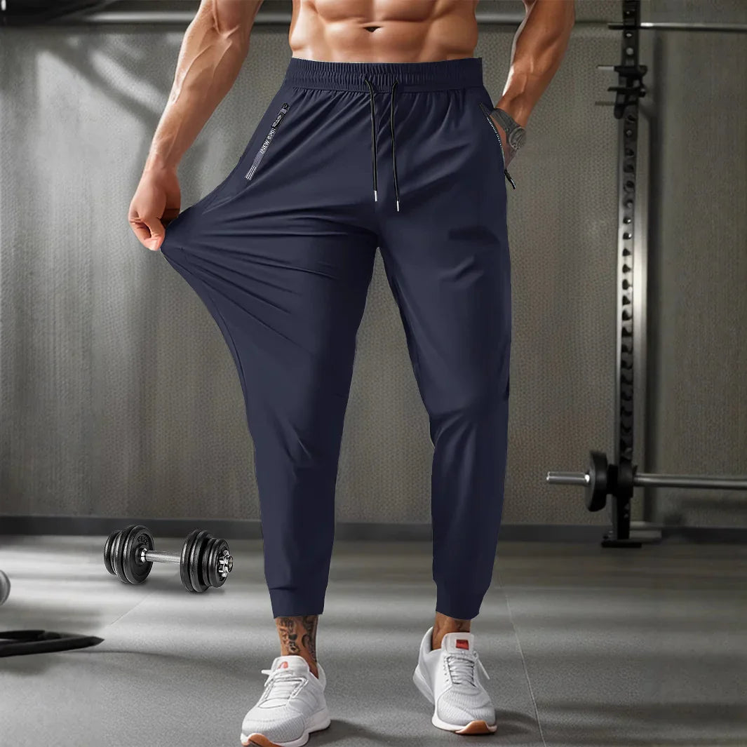 Athletic man stretching navy blue jogger pants in a gym setting with dumbbells and workout equipment
