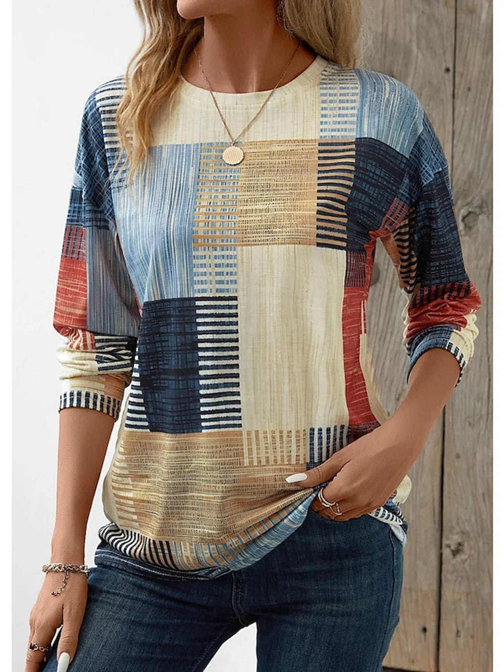 Woman wearing casual long-sleeve patchwork pattern top with blue jeans and gold necklace