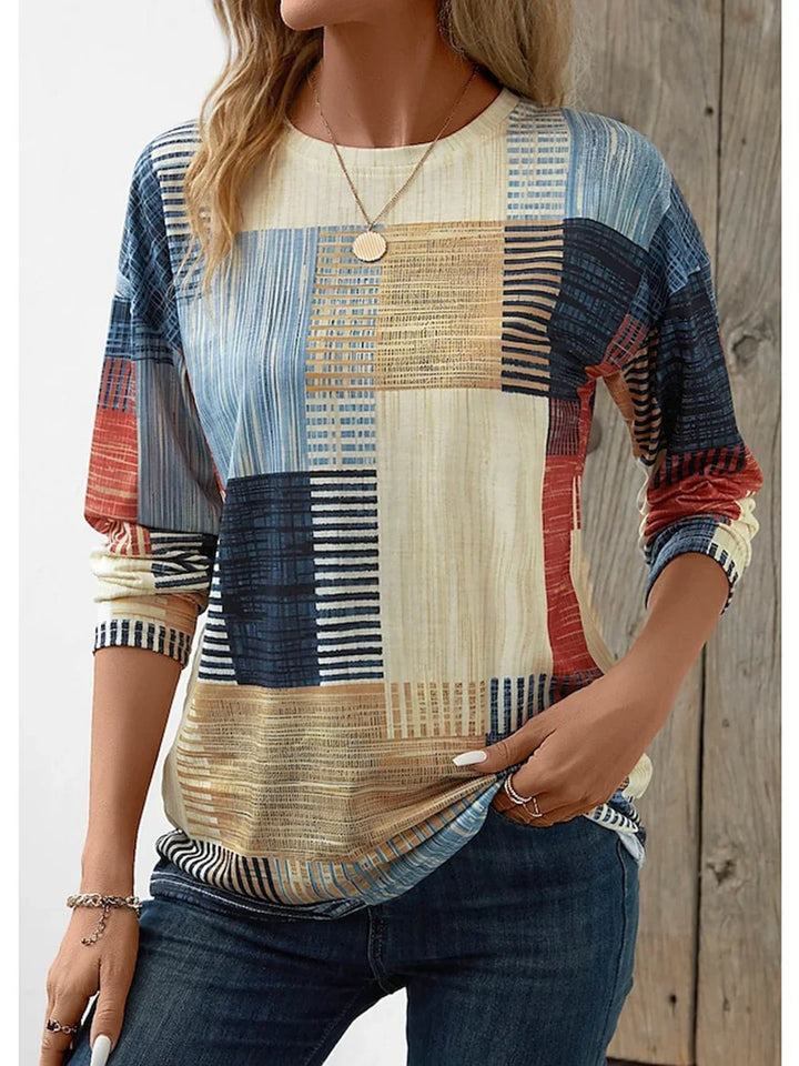 Woman wearing casual long-sleeve patchwork pattern top with blue jeans and gold necklace