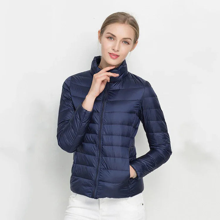 Woman wearing navy blue quilted lightweight puffer jacket and white pants against white background