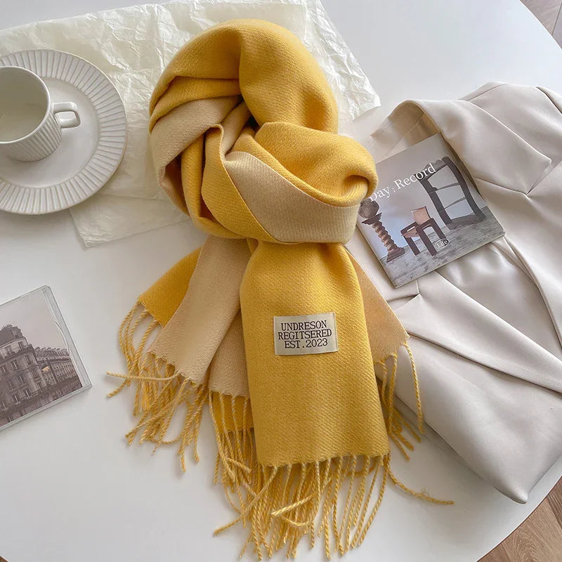 Yellow and beige fringed scarf with label on white table next to white blazer, coffee cup, and book