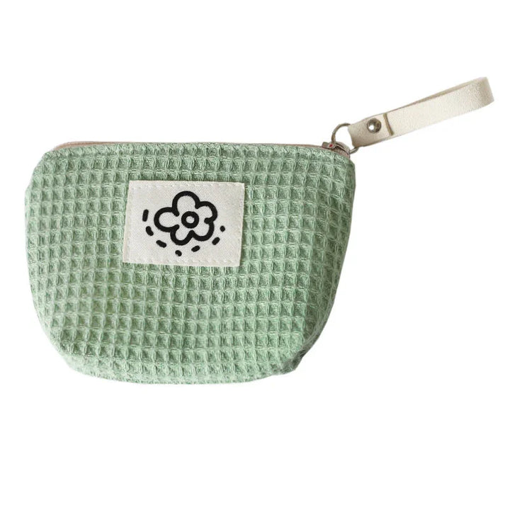 Light green waffle fabric wristlet pouch with a flower patch and beige zipper strap