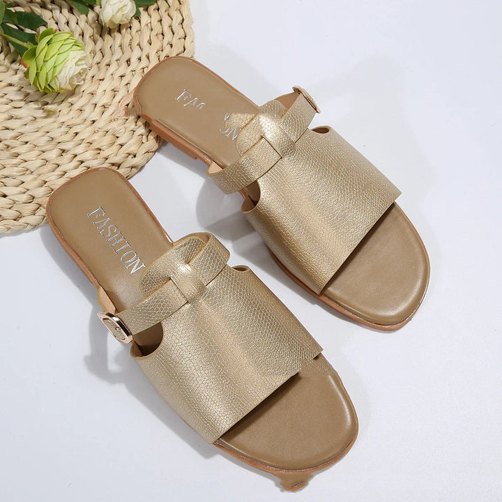 Pair of stylish gold leather flat sandals on white surface with woven mat and green flower