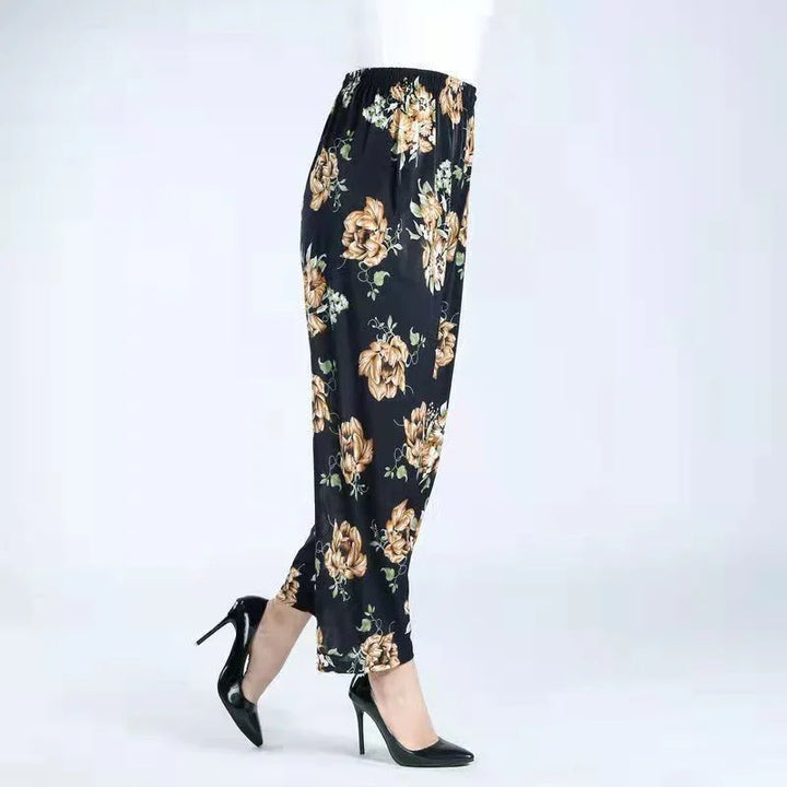 Side view of black floral print pants paired with black high heel shoes on white background