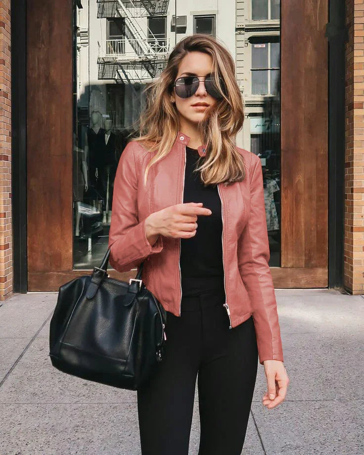 Stylish woman in pink leather jacket and sunglasses holding black handbag outside urban building