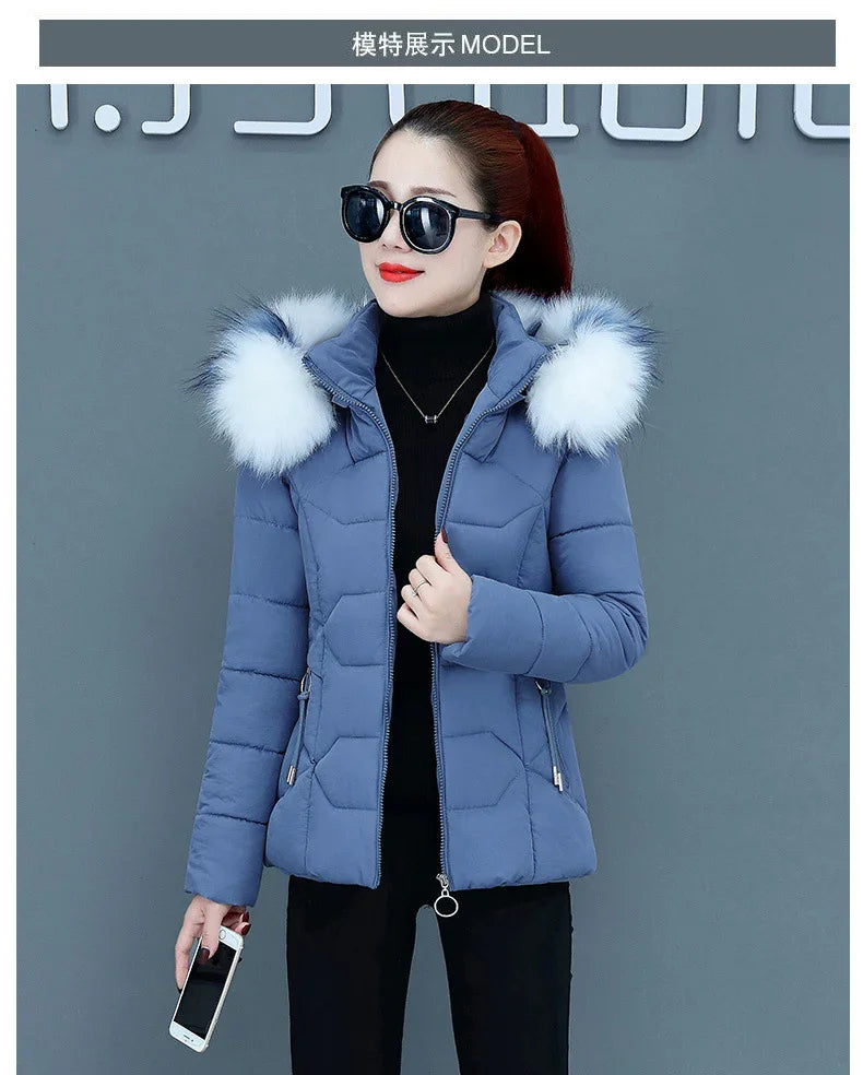 Woman wearing blue padded winter jacket with white fur hood and black sunglasses holding smartphone