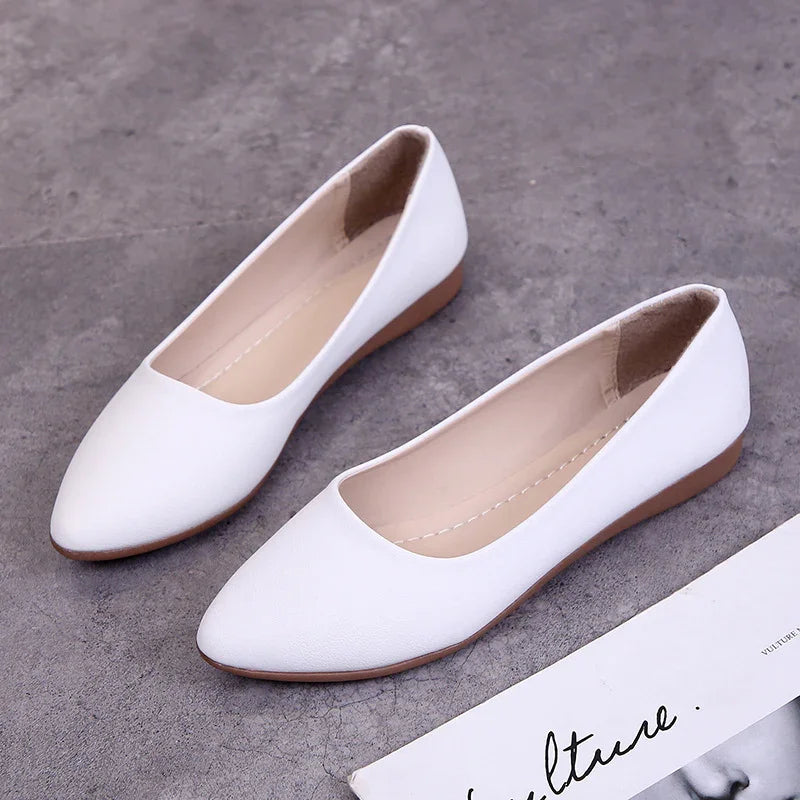 Pair of white pointed-toe flat shoes on gray concrete floor beside fashion magazine