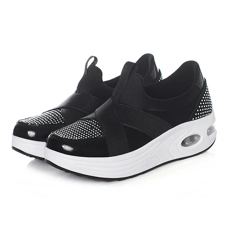Black slip-on sneakers with white soles and rhinestone embellishments on toe and heel